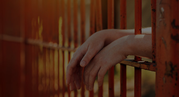 hands hanging between prison bars