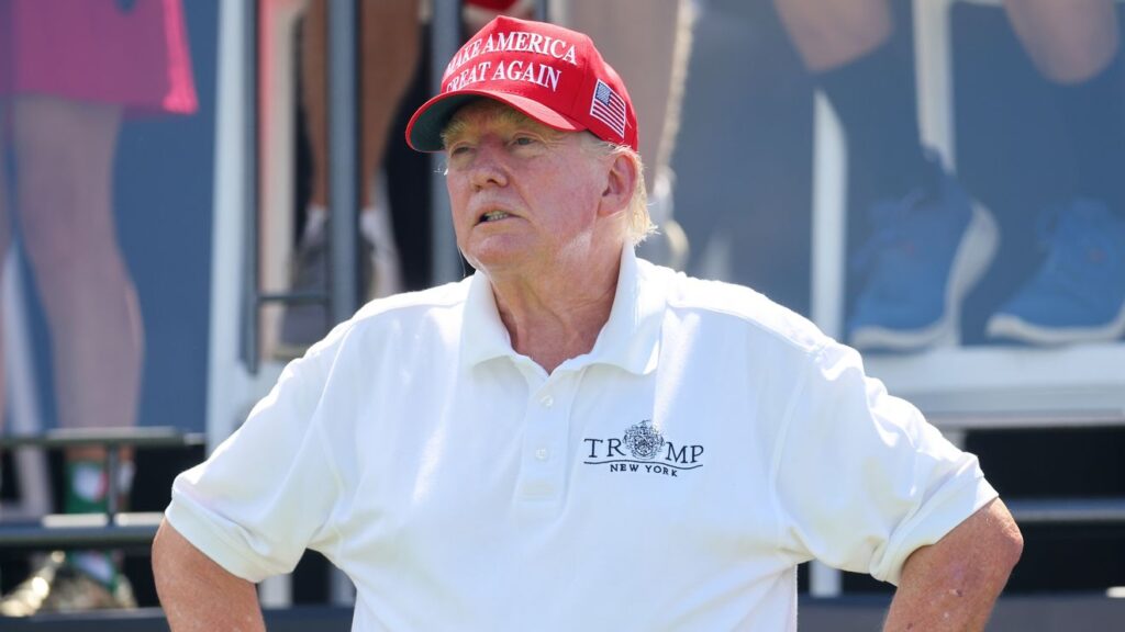 Donald Trump in red hat and white polo shirt at outdoor event
