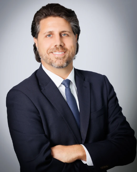 Florida criminal defense attorney Tyler DiMaio in a professional headshot, wearing a navy suit and tie with arms crossed and smiling against a light gray background